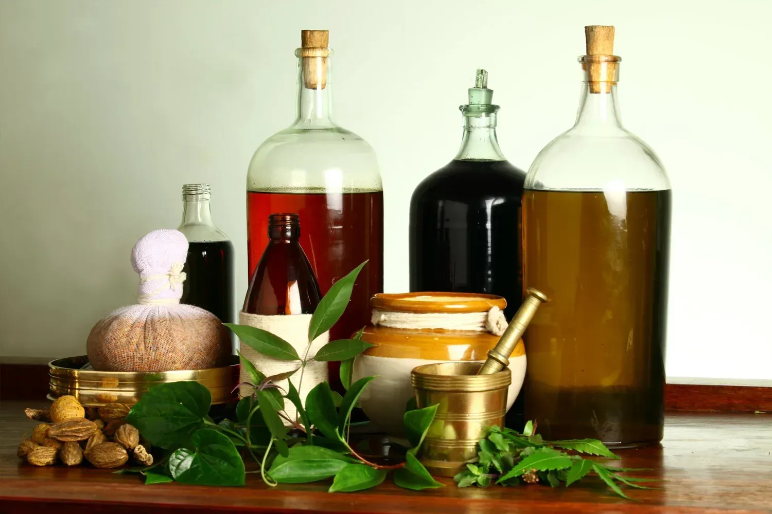 Bottles of Ayurvedic herbal oils with fresh leaves and a brass mortar
