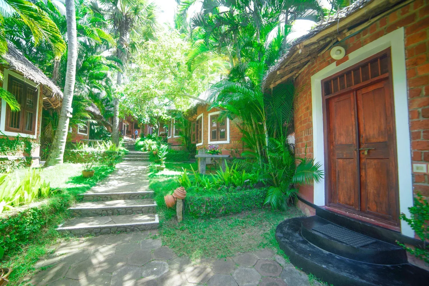 Brick cottage with a palm-thatched roof in the tropical garden at Manaltheeram