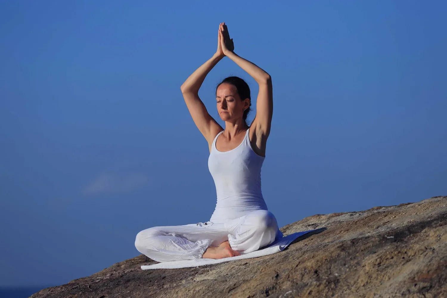 Woman meditating on a rock above the sea in Kerala
