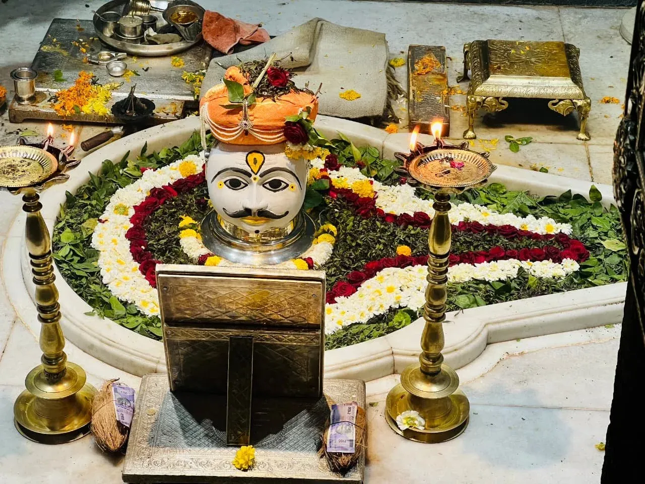 Flower-decorated shrine with brass oil lamps at a temple in India